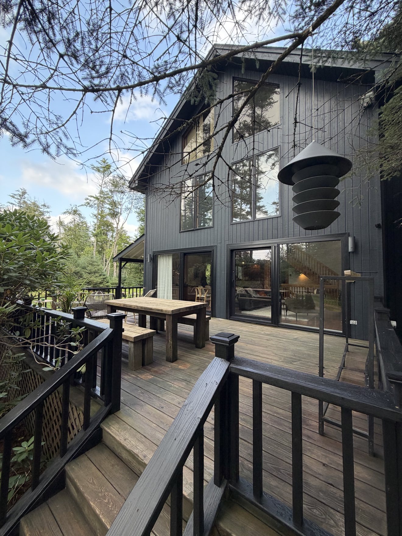 Black exterior of Lofty Cabin with a wooden dining table on the forest-facing deck